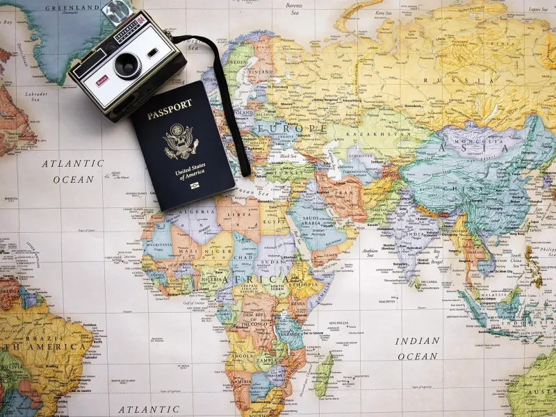 A world map with a camera, a jar of lipstick, and a United States passport on top.